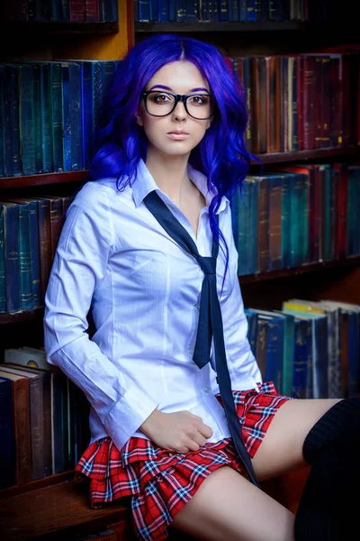 Pretty student girl with long purple hair posing in school clothes by the bookshelves.