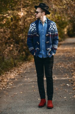 Tam uzunlukta hırka ve sonbahar doğa arka plan üzerinde açık duran şapka giymiş yakışıklı bir adam portresi. Sonbahar moda.