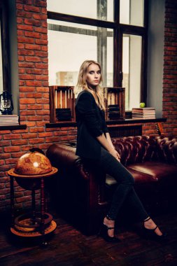 Çekici genç kadın deri kanepe tuğla duvarlı bir odada poz. Loft tarzı iç. Güzellik, moda. Akşam makyaj ve saç.