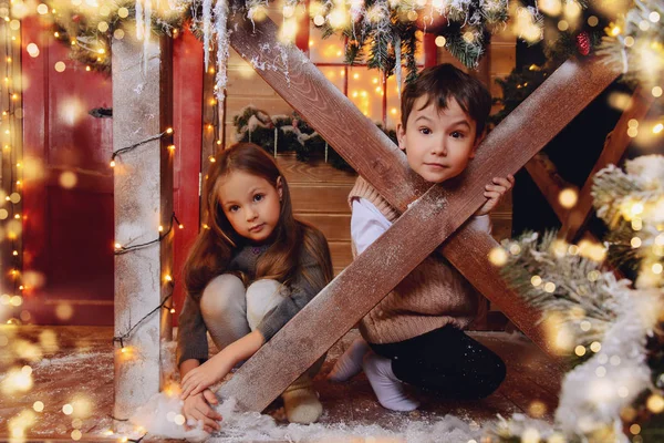 Cute brother and sister sit on the porch of a house decorated for Christmas. Merry Christmas and Happy New Year.