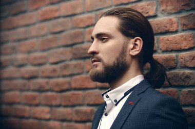 Erkek güzellik, moda. Zarif siyah takım elbise ve beyaz gömlek tuğla duvar tarafından poz yakışıklı delikanlı. Saç şekillendirme.