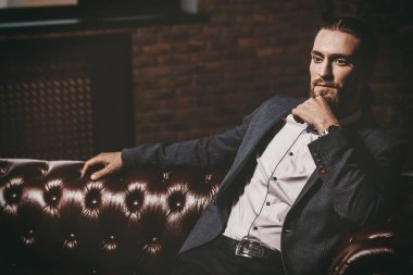 Modern bir iç bir deri kanepede oturan genç adam heybetli. Erkek güzelliği, moda.