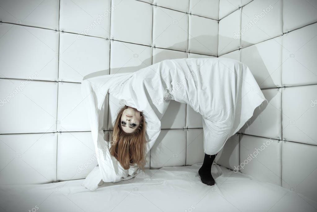 Portrait of a crazy girl dressed in a straitjacket in an isolated room in a madhouse.
