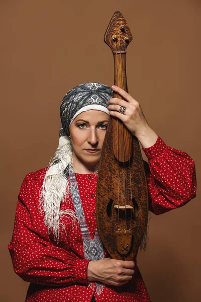 Elderly native woman in a national costume with ancient violin.