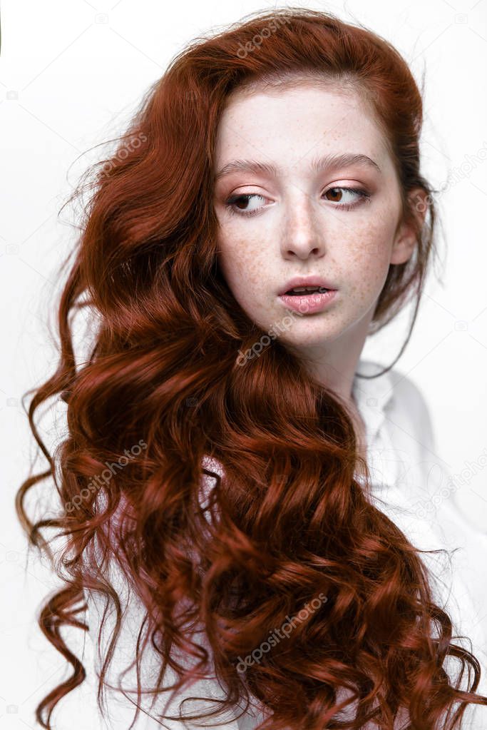 Close-up portrait of a  fifteen-year-old girl with long curly red hair over white background. Beauty, fashion.