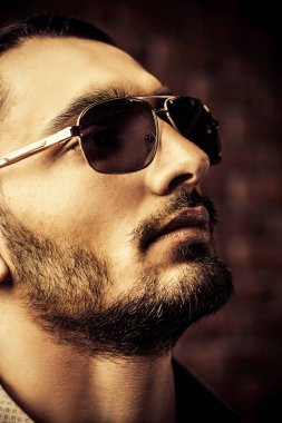Yakın çekim portre yakışıklı bir brunet erkek güneş gözlüğü üzerinde tuğla duvar arka plan. Erkek güzelliği, moda. Erkek Berber Dükkanı, saç modeli.