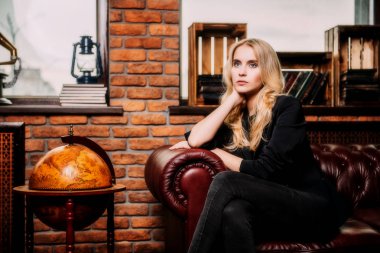 Çekici genç kadın deri kanepe tuğla duvarlı bir odada poz. Loft tarzı iç. Güzellik, moda. Akşam makyaj ve saç.