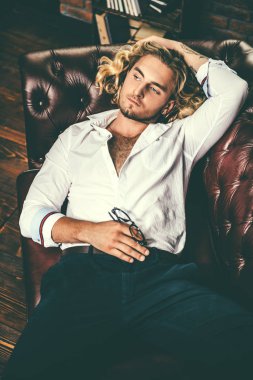 Seksi yakışıklı genç bir koltukta yalan Beyaz gömlekli. Erkek güzelliği, moda. Saç, saç modeli.