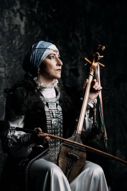 Yaşlı yerli kadın ulusal bir kostüm. Antik keman çalıyor.