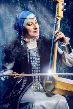 Yaşlı yerli kadın ulusal bir kostüm. Antik keman çalıyor.