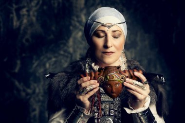 Yaşlı yerli kadın. Ulusal bir kostüm. Reedpipe oynuyor.