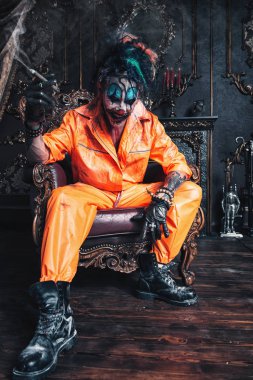 Şeytani palyaço adam kan lekeli bir odada vintage iç puro ile oturuyor. Cadılar Bayramı. Korku, gerilim filmi.