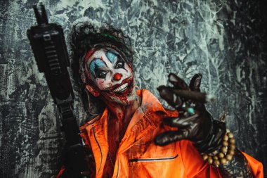 Deli şeytani palyaço adam kan lekeli bir puro sigara ve elinde bir silah. Cadılar Bayramı. Korku, gerilim filmi.