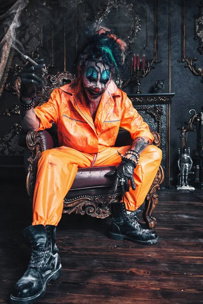 Şeytani palyaço adam kan lekeli bir odada vintage iç puro ile oturuyor. Cadılar Bayramı. Korku, gerilim filmi.
