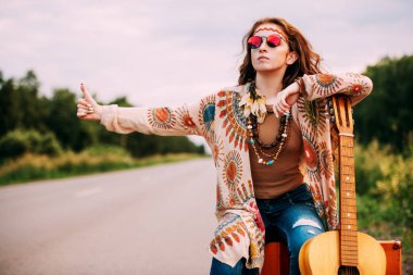 Hitchhiking girl. Beautiful hippie girl standing on a highway and catching a passing car. Spirit of freedom. Fashion shot. Bohemian, bo-ho style. clipart