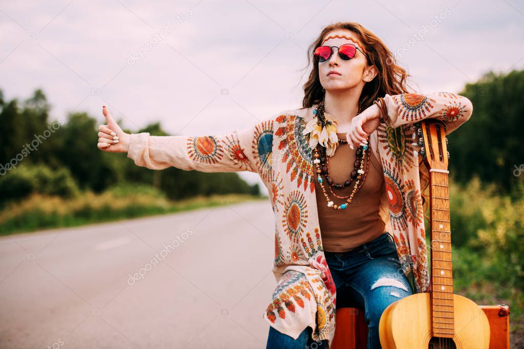 Hitchhiking girl. Beautiful hippie girl standing on a highway and catching a passing car. Spirit of freedom. Fashion shot. Bohemian, bo-ho style.