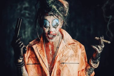 Deli şeytani palyaço adam kan lekeli bir puro sigara ve elinde bir silah. Cadılar Bayramı. Korku, gerilim filmi.