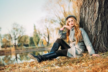Romantik genç kadın güzel bir sonbahar park ağacın altında oturuyor. Güzellik, sonbahar moda.
