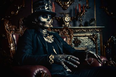 Halloween. A man with a skull makeup dressed in a tail-coat and a top-hat is in the old castle. Baron Saturday. Baron Samedi. Dia de los muertos. Day of The Dead. Old vintage interior. clipart