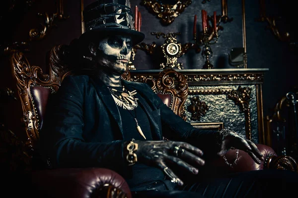 Halloween. A man with a skull makeup dressed in a tail-coat and a top-hat is in the old castle. Baron Saturday. Baron Samedi. Dia de los muertos. Day of The Dead. Old vintage interior.