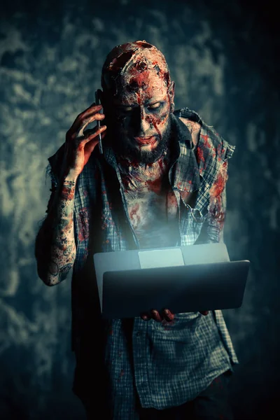 Creepy scary zombie is talking on the phone with a laptop. Halloween. Horror film.