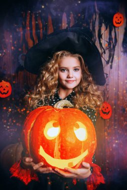 Sevimli kıvırcık kız kostümlü bir cadı balkabağı fener tutar. Cadılar Bayramı partisi. 