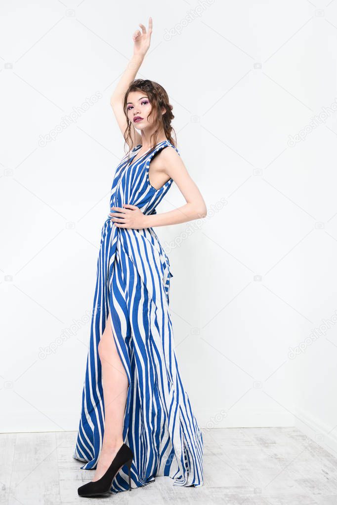 Beautiful attractive girl wearing striped long dress posing in studio. Beauty, fashion. Studio shot. Full length portrait.