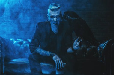 Bir vampir adam kanepede oturan ve bir siyah kuzgun tutarak. Cadılar Bayramı gecesi. Güzellik, moda.