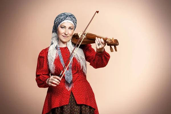 Elderly native woman in a national costume plays the ancient violin.