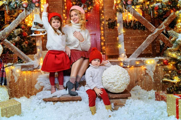 Happy mom and children are posing near the house, decorated for Christmas. Seasonal winter fashion. Merry Christmas and Happy New Year.