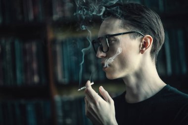 Düşünceli ve sakin bir şekilde sigara çekici bir genç adam. Erkek güzelliği, moda. Optik stili.