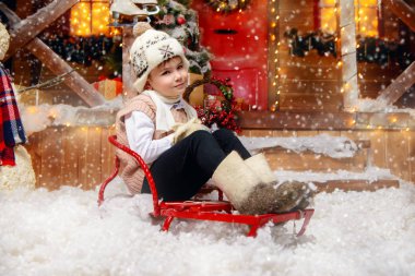 Sevimli küçük çocuk kış giysileri ve bir şapka kızak Noel Baba'nın sihirli evin önünde oturur. Mucize zamanı. Mutlu Noeller ve mutlu yeni yıl.