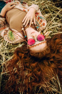 A portrait of a fashion female model lying on the grass. Contemporary bohemian style. Spirit of freedom. Fashion shot. Bohemian, bo-ho style. clipart