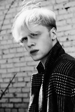 Bir şehir sokak bir tuğla bina üzerinde duran bir ekose ceket giymiş sarışın saçlı yakışıklı bir genç adam portresi. Erkek güzellik ve sağlık. Güzellik, şehir moda. Siyah beyaz resim.