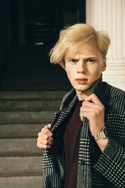 Sarı saçlı bir şehir sokakta duran ekose bir palto giyiyor ile yakışıklı bir genç adam portresi. Erkek güzellik ve sağlık. Güzellik, şehir moda.