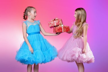 İki sevimli küçük kız ellerinde hediye kutuları ile güzel festival elbiseler giymiş. Çocuk moda kavramı.
