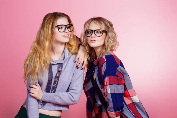 Studio bardaklarda pembe arka plan üzerinde poz iki neşeli genç kadın. Güzellik, kış modası. Gençlik tarzı. Tam uzunlukta portre. 