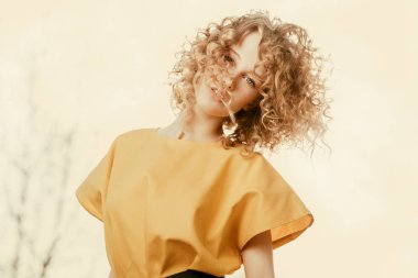 Sarı elbiseli kıvırcık saçlı çekici bir genç kızın portresi. Moda, güzellik.