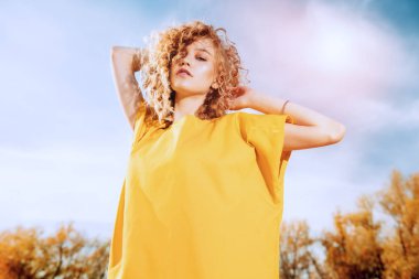 Sarı elbiseli kıvırcık saçlı çekici bir genç kızın portresi. Moda, güzellik.