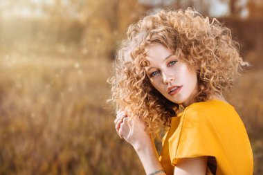 Sarı elbiseli kıvırcık saçlı çekici bir genç kızın portresi. Moda, güzellik.