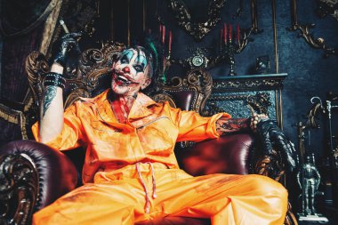 Şeytani palyaço adam kan lekeli bir odada vintage iç puro ile oturuyor. Cadılar Bayramı. Korku, gerilim filmi.