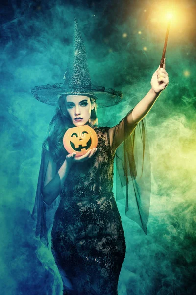 A witch holding a magic stick and a pumpkin. Halloween. Celebration.