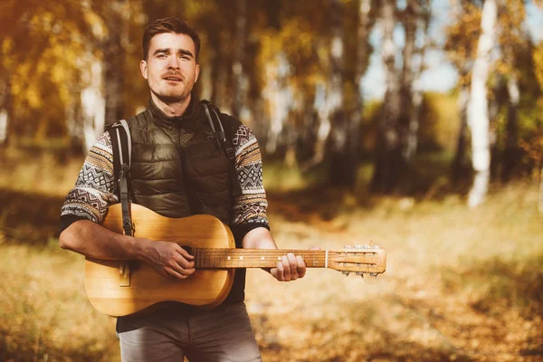 A handsome man in countryside with a guitar. Autumn fashion for men. Freedom, lifestyle.