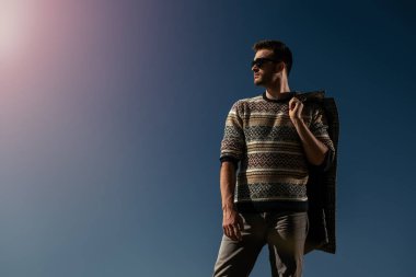 Bir ceket içinde güneş gözlüğü tutan yakışıklı acımasız bir adam. Moda Erkekler için. Sonbahar, kış.