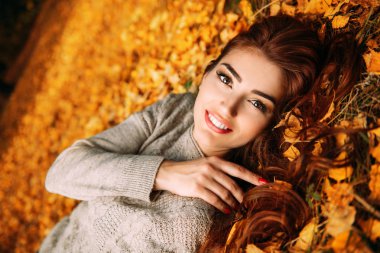 Altın sonbahar yapraklarıyla yerde yatan güzel bir genç kadının portresi. Yaşam tarzı, sonbahar modası, güzellik. 