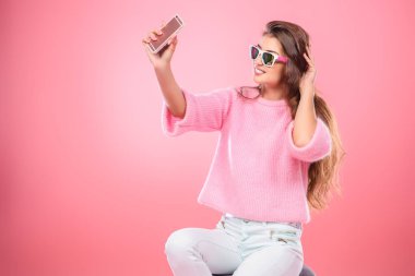 Pembe arka plan üzerinde selfie yapma smartphone ile poz güzel ve şirin bir genç bayan portresi. Moda, gadget'lar ve elektronik kavramı.