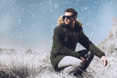 Kırsal kesimde bir parka ve güneş gözlüğü takan yakışıklı acımasız bir adam. Moda Erkekler için. Sonbahar, kış.