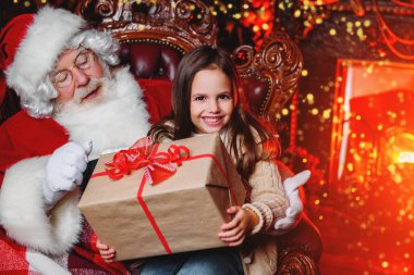 Mutlu bir genç kız Noel Baba yakınındaki bir hediye ile evde oturuyor. Mutlu Noeller ve mutlu yeni yıl.