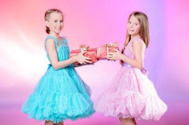 İki sevimli küçük kız ellerinde hediye kutuları ile güzel festival elbiseler giymiş. Çocuk moda kavramı.