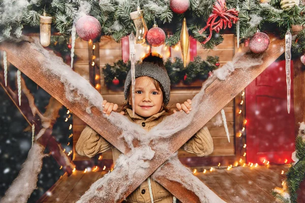 A little boy sitting on the porch of the house decorated for Christmas. Miracle time. Merry Christmas and Happy New Year.